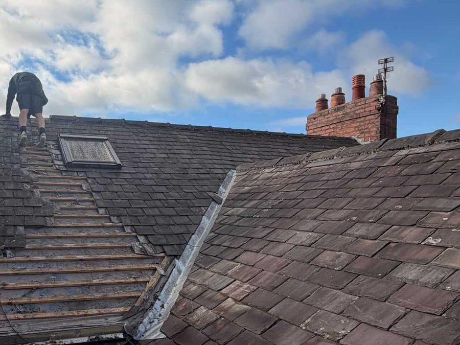 Roof stripped back to the battens with a roofer working at the ridge