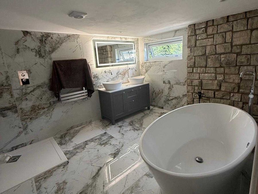 Freestanding bath against an exposed stone wall in a marble bathroom